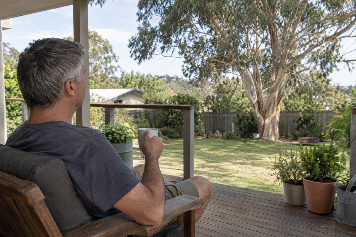 A man relaxing on a back deck with a cup of coffee, looking out over the garden