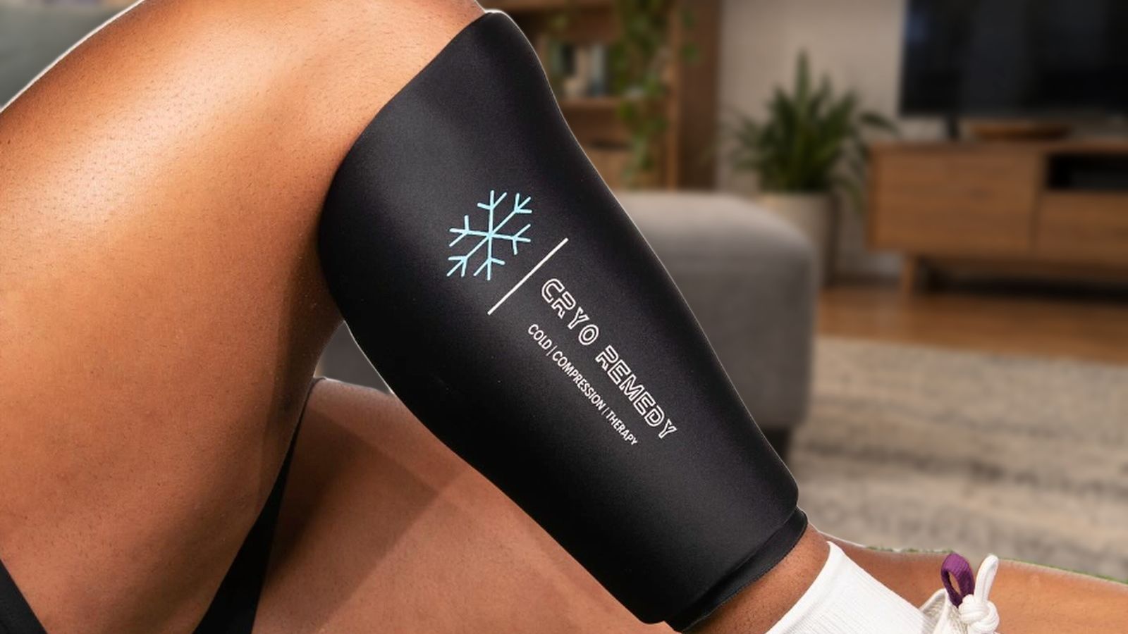 A black Cryo Remedy compression sleeve on a calf, a lounge room out of focus behind